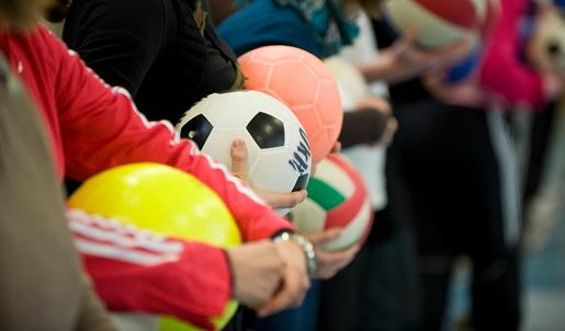 Ein Fußball, ein orangener Ball und ein gelber Ball werden von unterschiedliche Personen gehalten, die in einer Reihe stehen.
