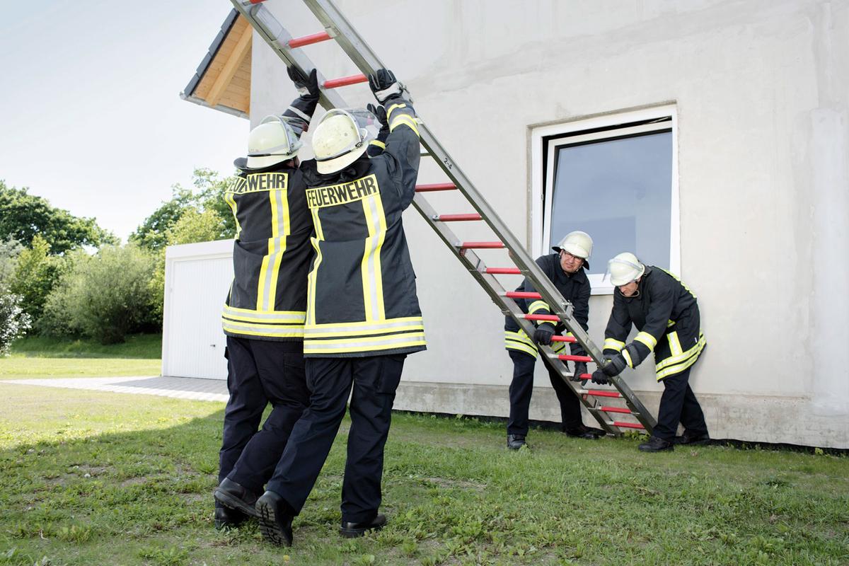 Öffnet eine Lightbox: Vier Feuerwehrleute stellen eine Leiter an einer Hauswand auf