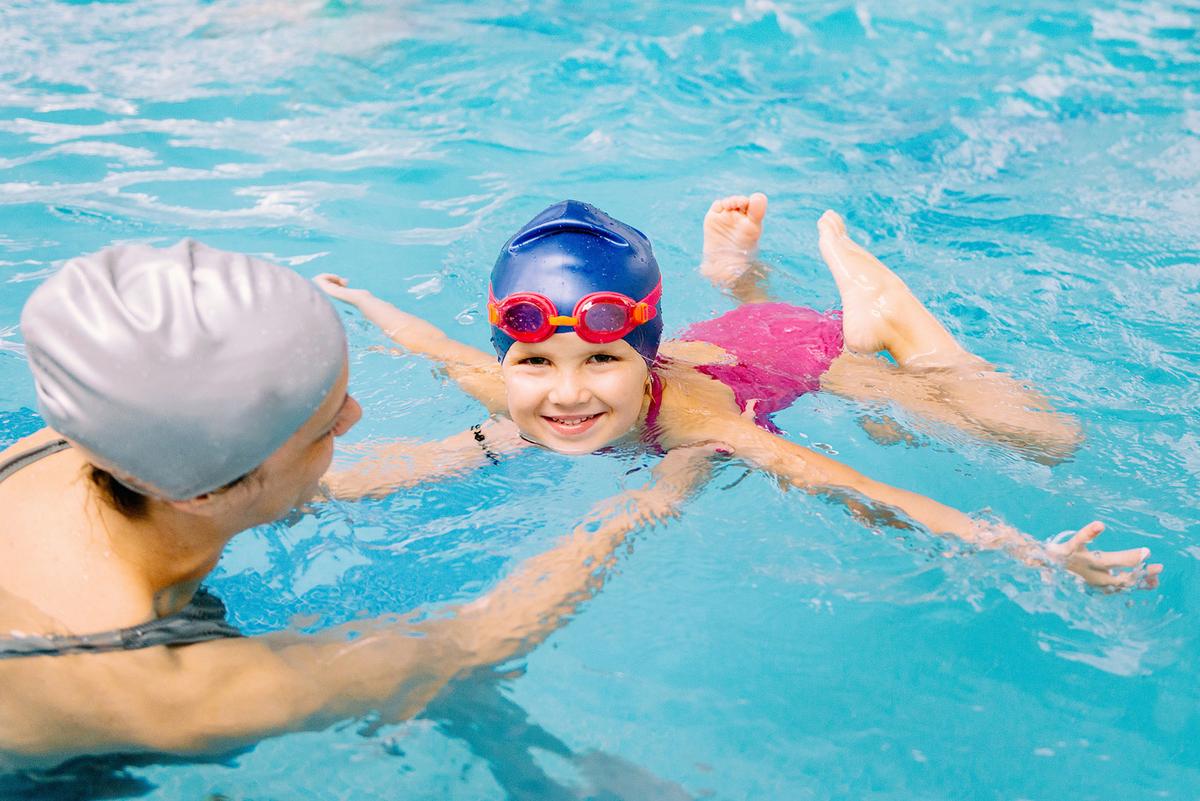 Großansicht: Eine Frau bringt einem Grundschulkind das Schwimmen bei.