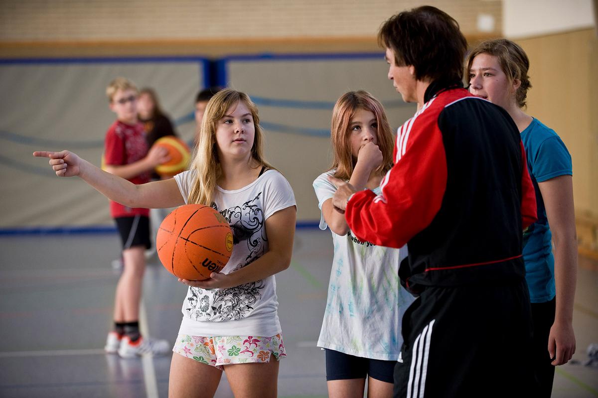 Öffnet eine Lightbox: Eine Sportlehrerin unterhält sich mit drei Schülerinnen.