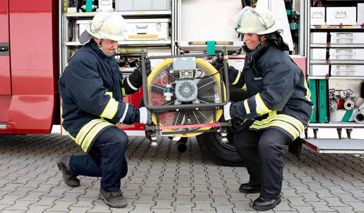 Ein Feuerwehrmann und eine Feuerwehrfrau entnehmen ein Belüftungsgerät aus dem Feuerwehrwagen.