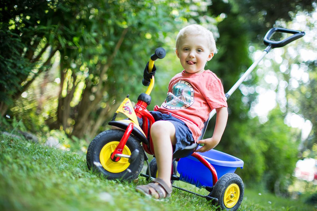 Großansicht: Ein Kleinkind steht mit seinem Dreirad auf der Wiese.