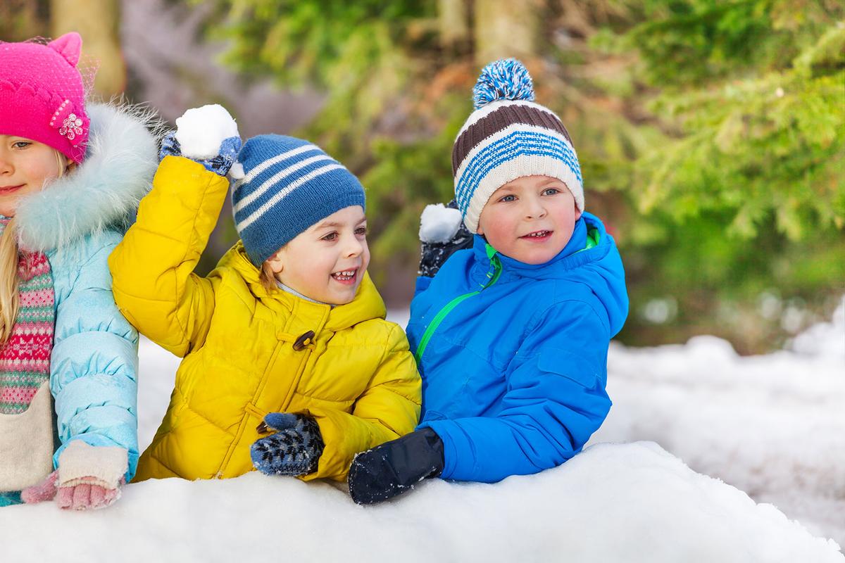 Öffnet eine Lightbox: Drei Kinder hocken in Winterkleidung im Schnee. Zwei der Kinder werfen mit Schneebällen.
