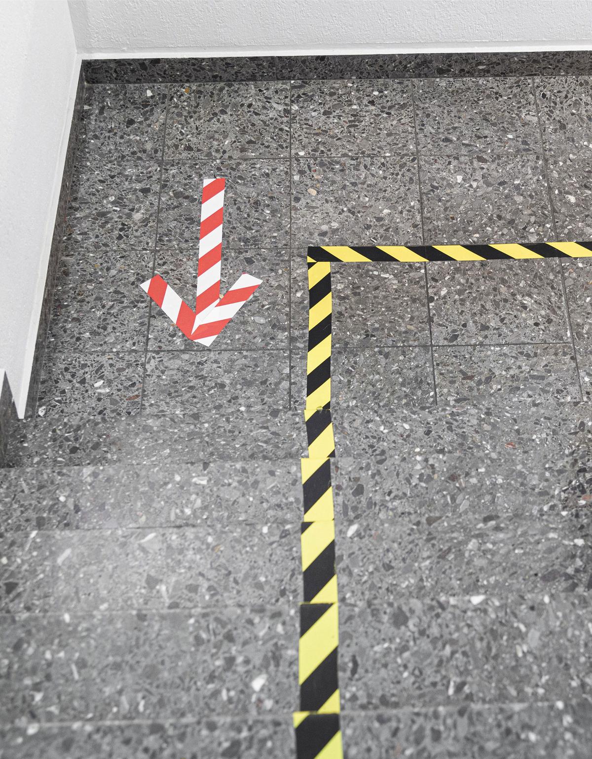 Großansicht: Auf dem Boden wurden Laufwege mit schwarz-gelbem Klebeband abgeklebt und rot-weiße Pfeile zeigen die jeweilige Laufrichtung an. 