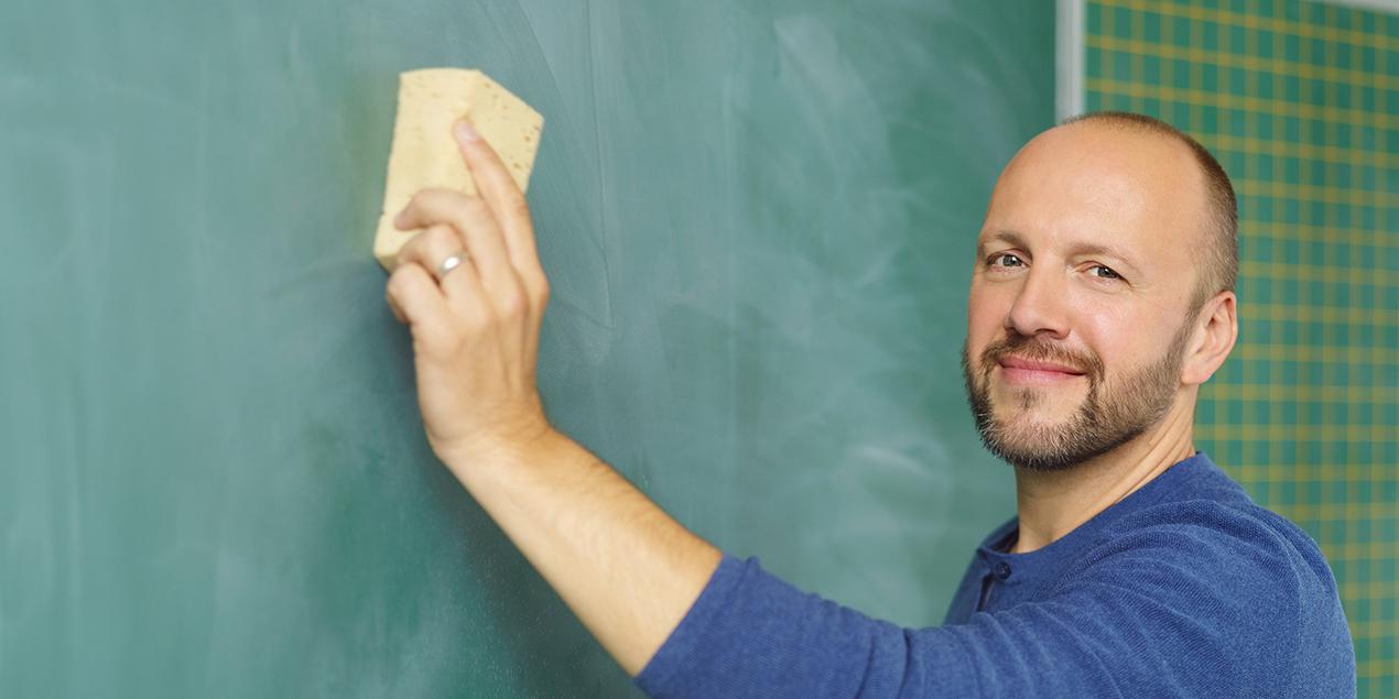 Ein junger Lehrer wischt die Schultafel mit einem Schwamm