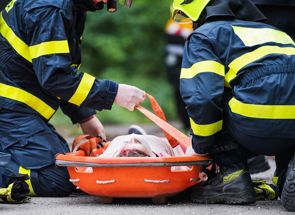 Großansicht: Zwei Einsatzkräfte der Feuerwehr sichern eine Patientin auf einer Trage.