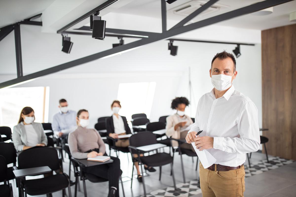 Öffnet eine Lightbox: Ein Referent steht vor Seminarteilnehmer*innen, alle tragen eine Maske