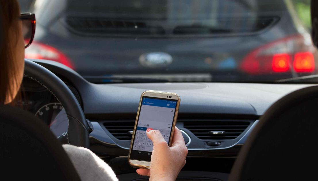 Öffnet eine Lightbox: Die Fahrerin benutzt ein Smartphone beim Fahren.