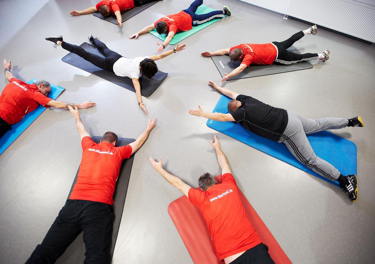 Öffnet eine Lightbox: Betriebliche Gesundheitsförderung: Mehrere Personen trainieren auf Sportmatten.