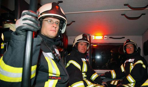 Drei Feuerwehrleute in Schutzkleidung sitzen im Fond eines Feuerwehr-LKW