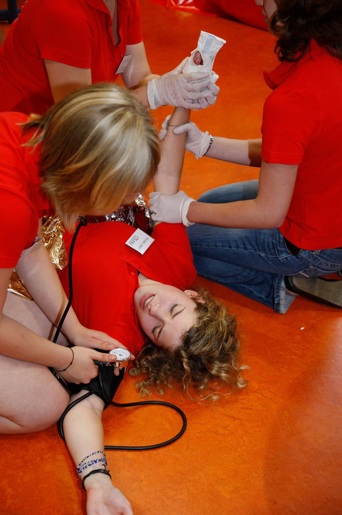 Großansicht: Schulsanitäter üben an einem Mitglied Erste-Hilfe Maßnahmen. Dabei benutzen sie eine Blutdruckmanschette um den Puls zu messen.