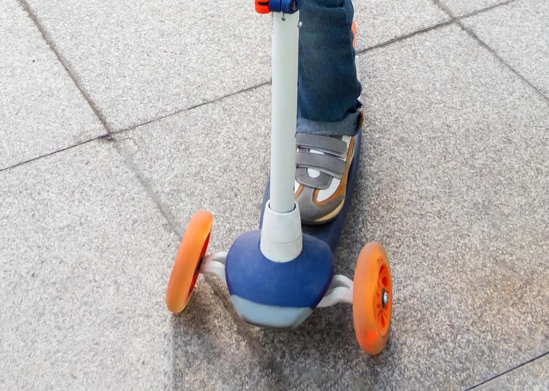Ein Junge mit Helm f&auml;hrt mit einem Roller.
