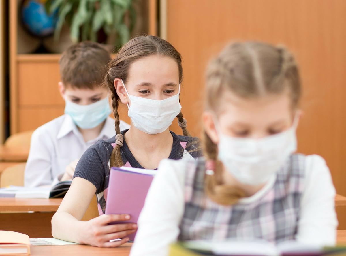 Schulkinder mit Medizinmaske im Gesicht im Klassenzimmer.