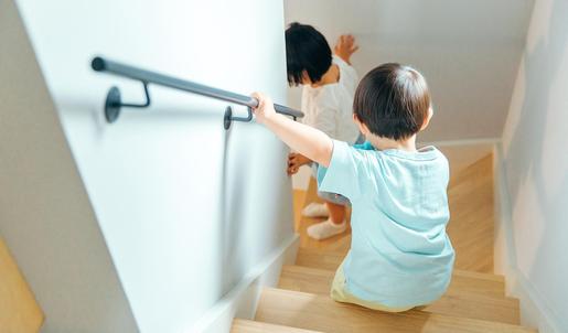 Ein Kind folgt einer erwachsenen Frau die Treppe hinunter und hält sich dabei am Treppengeländer fest.