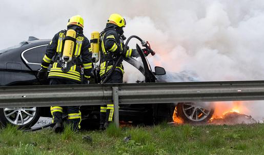 Zwei Feuerwehrangehörige löschen ein brennendes Auto.