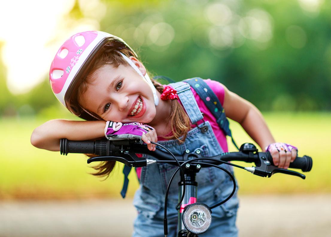 Ein M&auml;dchen mit Helm und fingerlosen Handschuhen sitzt auf einem Fahrrad.