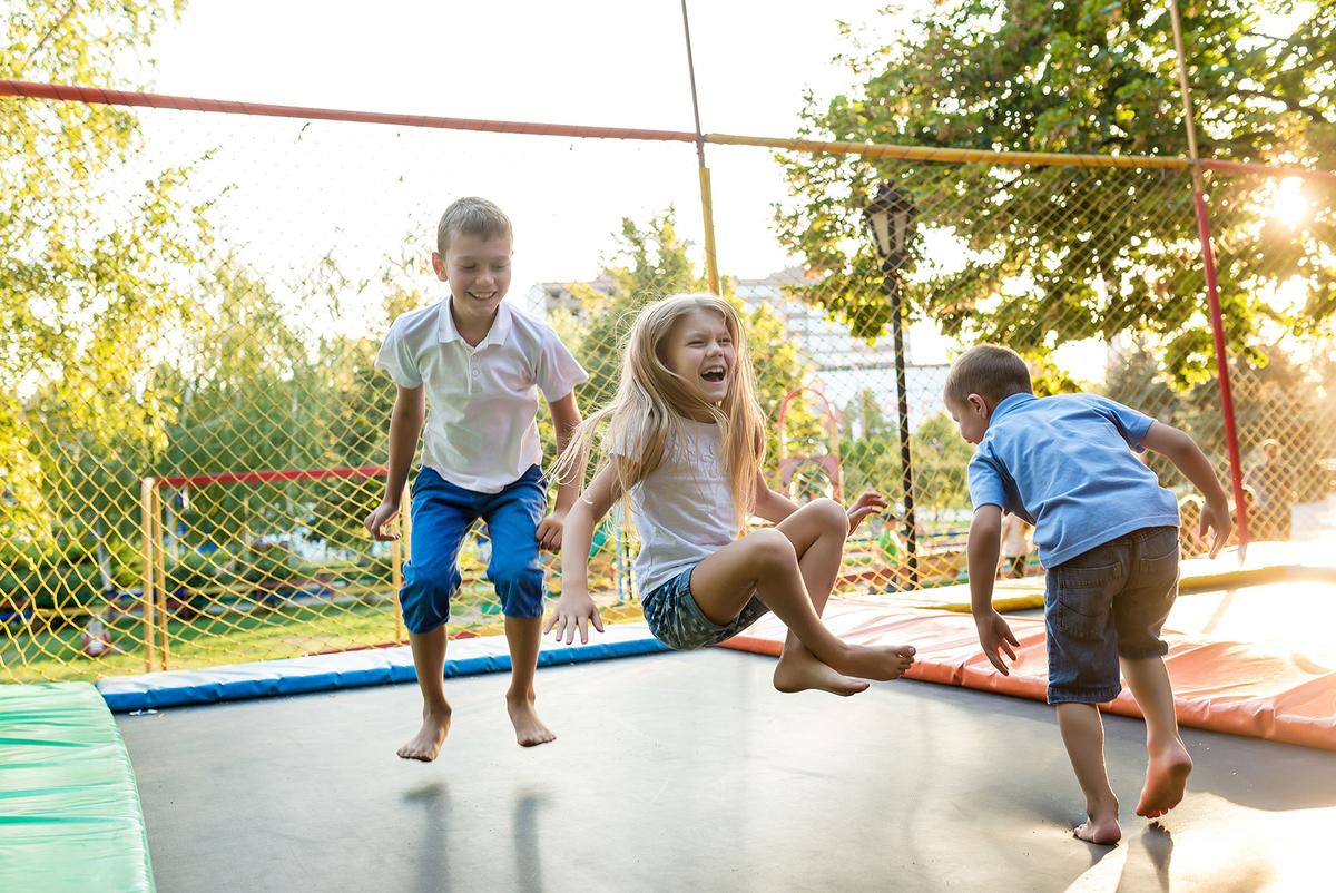 Großansicht: Zwei Jungen und ein Mädchen hüpfen freudig auf einem Trampolin.