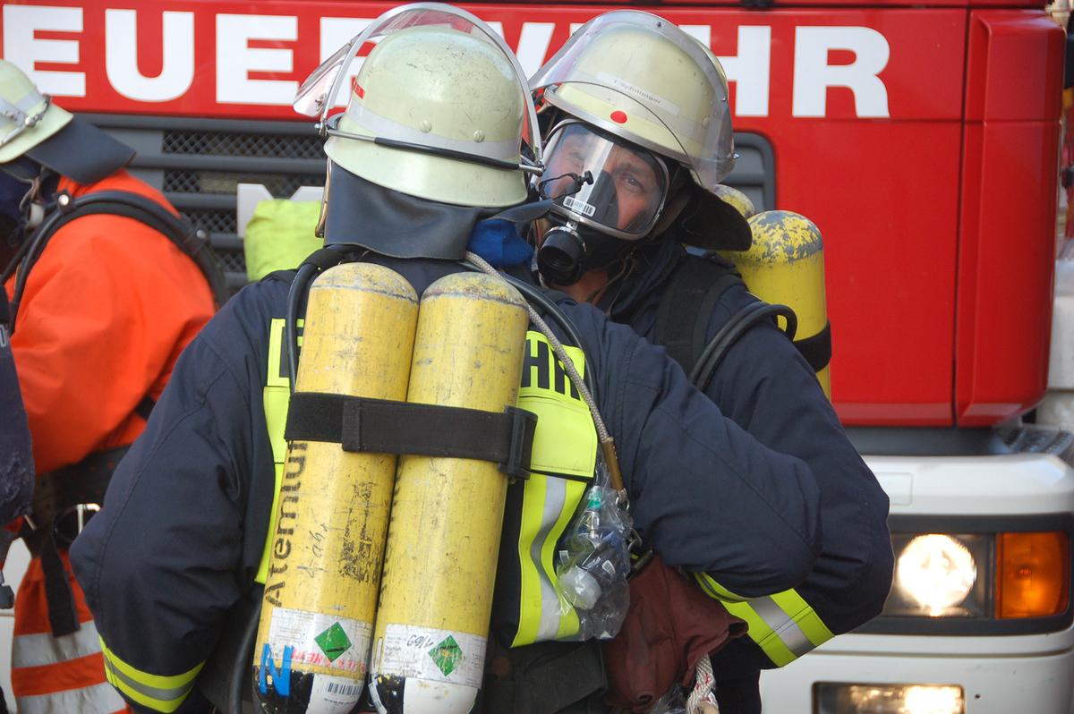 Großansicht: Feuerwehrmänner mit Atemschutzmasken stehen vor einem Feuerwehrwagen.