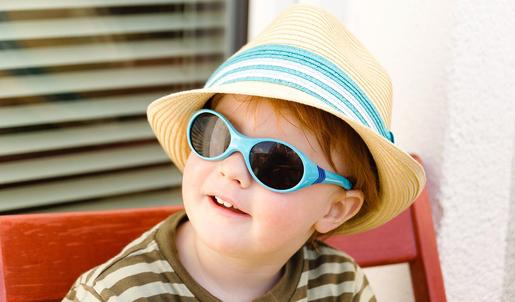 Ein Kind trägt einen Sonnenhut und eine Sonnenbrille um sich vor der Sonne zu schützen.