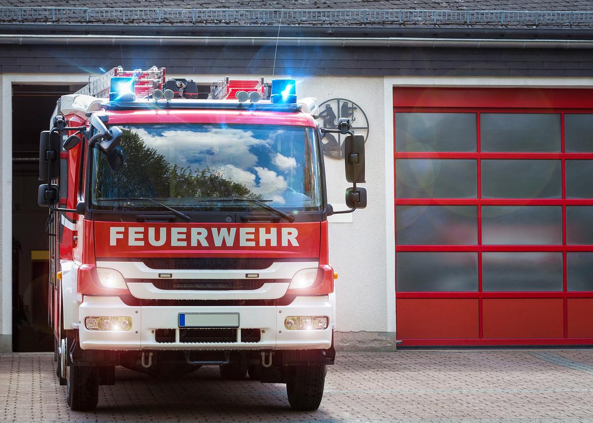 Öffnet eine Lightbox: Ein Löschfahrzeug fährt mit Blaulicht aus einer Fahrzeughalle der Feuerwehr.