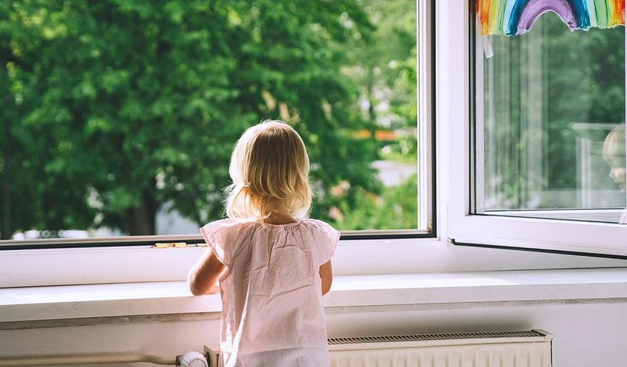 Ein kleines Mädchen schaut durch ein geöffnetes Kita-Fenster in den Garten